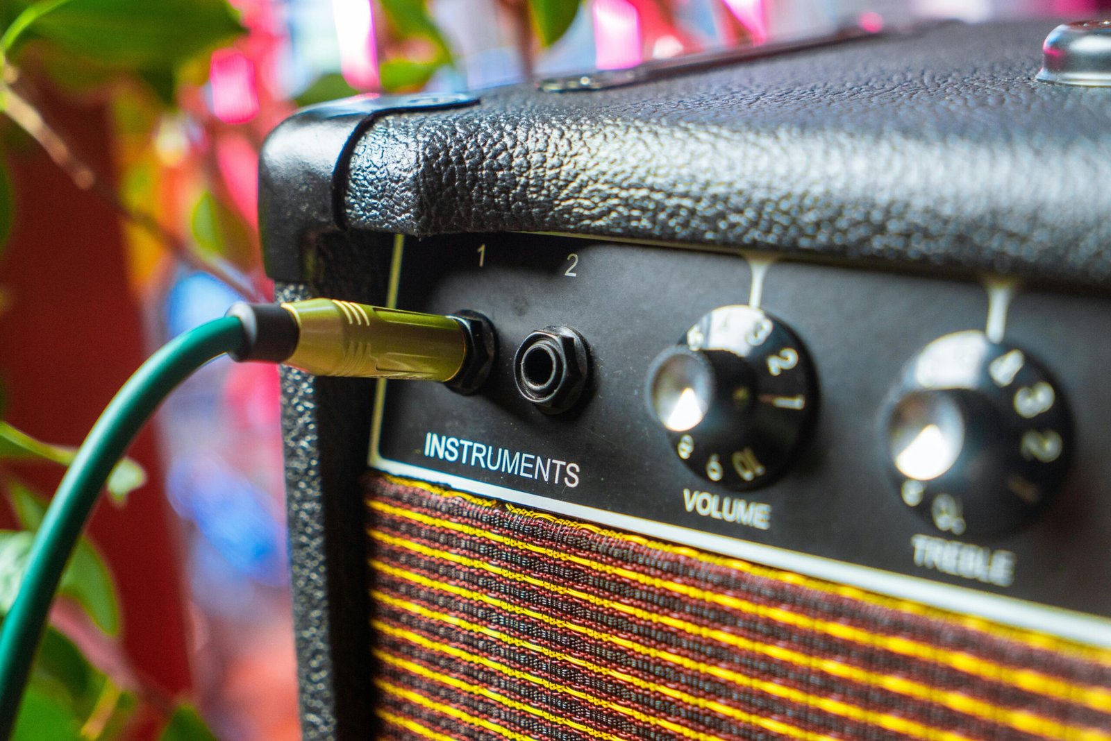 Detailed close-up of an amplifier with an instrument cable plugged into the input, showcasing volume and treble knobs.